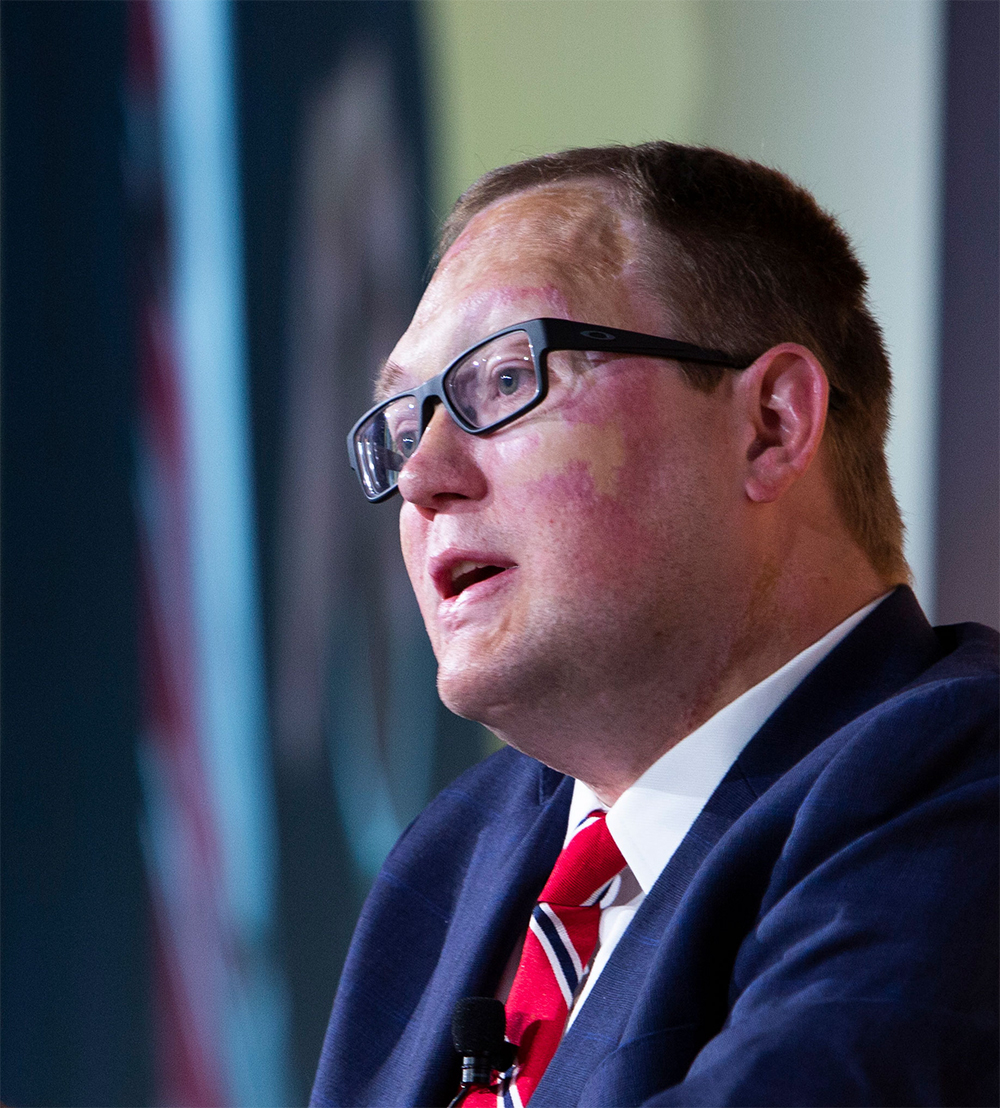 Headshot of John Morris wearing a blue suit, white shirt and red tie.